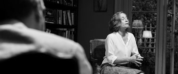 Movie still from “The Party” (2017), directed by Sally Potter – A woman sitting in a chair in front of a book shelf; Medium shot, Over the shoulder angle