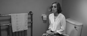 Movie still from “The Party” (2017), directed by Sally Potter – A black and white photo of a woman sitting in front of a towel rack; Medium shot, Over the shoulder angle