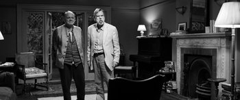 Movie still from “The Party” (2017), directed by Sally Potter – Two men standing in front of a piano in a living room; Wide shot, Over the shoulder angle