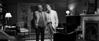 Movie still from “The Party” (2017), directed by Sally Potter – Two men standing next to each other in front of a piano; Wide shot, Over the shoulder angle