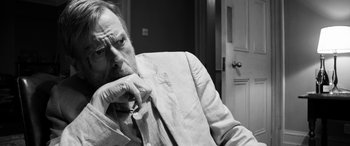 Movie still from “The Party” (2017), directed by Sally Potter – An older man sitting in a chair with his chin resting on his hand; Close Up shot, Over the shoulder angle