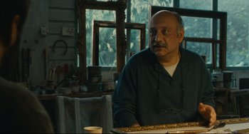 Movie still from “The Past” (2013), directed by Asghar Farhadi – A man sitting at a table in front of a painting; Medium shot, Low angle