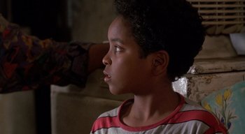 Movie still from “The People Under the Stairs” (1991), directed by Wes Craven – A young boy is sitting in front of a wall; Close Up shot, Over the shoulder angle