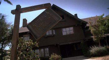 Movie still from “The People Under the Stairs” (1991), directed by Wes Craven – A sign hanging off the side of a building; Wide shot, Low angle