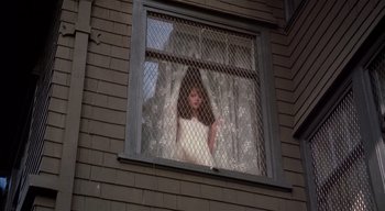 Movie still from “The People Under the Stairs” (1991), directed by Wes Craven – A woman in a white dress looking out of a window; Wide shot, Low angle