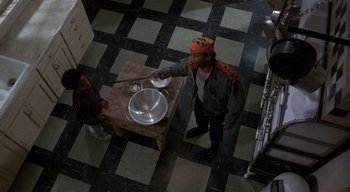 Movie still from “The People Under the Stairs” (1991), directed by Wes Craven – A man standing in front of a table with a bowl on it; Medium shot, High angle