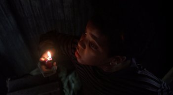 Movie still from “The People Under the Stairs” (1991), directed by Wes Craven – A young boy holding a lit candle in a dark room; Close Up shot, High angle