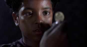 Movie still from “The People Under the Stairs” (1991), directed by Wes Craven – A young man holding a coin in his hand; Close Up shot, Over the shoulder angle