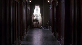 Movie still from “The People Under the Stairs” (1991), directed by Wes Craven – A hallway with a chair , lamp , and a window; Wide shot, High angle