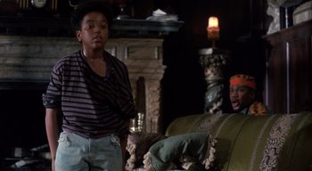 Movie still from “The People Under the Stairs” (1991), directed by Wes Craven – Two people in a living room with a fireplace in the background; Medium shot, Over the shoulder angle