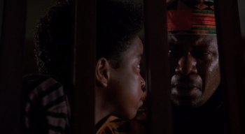 Movie still from “The People Under the Stairs” (1991), directed by Wes Craven – A young boy looking out of a window at an older man; Close Up shot, Over the shoulder angle