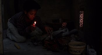 Movie still from “The People Under the Stairs” (1991), directed by Wes Craven – A boy is lighting a candle in the dark; Medium shot, High angle