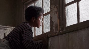 Movie still from “The People Under the Stairs” (1991), directed by Wes Craven – A young boy looking out of a broken window; Close Up shot, Low angle