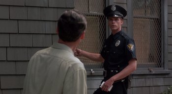 Movie still from “The People Under the Stairs” (1991), directed by Wes Craven – A police officer is pointing to a man's shirt; Medium shot, Over the shoulder angle