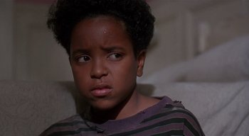 Movie still from “The People Under the Stairs” (1991), directed by Wes Craven – A young black boy sitting on top of a white couch; Close Up shot, High angle