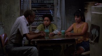 Movie still from “The People Under the Stairs” (1991), directed by Wes Craven – A group of people sitting at a wooden table; Medium shot, High angle