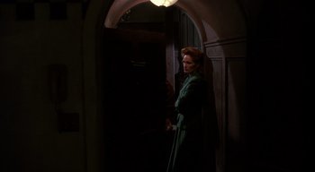 Movie still from “The People Under the Stairs” (1991), directed by Wes Craven – A woman standing in a dark room with a light shining on her head; Medium shot, Low angle