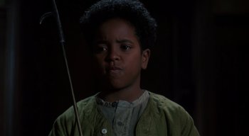 Movie still from “The People Under the Stairs” (1991), directed by Wes Craven – A young boy holding a stick in a dark room; Close Up shot, High angle