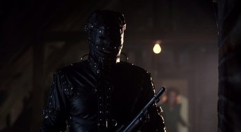 Movie still from “The People Under the Stairs” (1991), directed by Wes Craven – A man in a black leather outfit holding a gun; Medium shot, Low angle