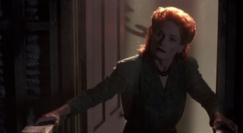 Movie still from “The People Under the Stairs” (1991), directed by Wes Craven – A woman with red hair is standing in a doorway; Medium shot, High angle