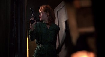 Movie still from “The People Under the Stairs” (1991), directed by Wes Craven – A woman holding a gun while standing next to a wall; Medium shot, Low angle