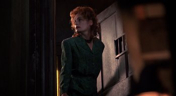 Movie still from “The People Under the Stairs” (1991), directed by Wes Craven – A woman in a green suit standing in a dark room; Medium shot, Low angle