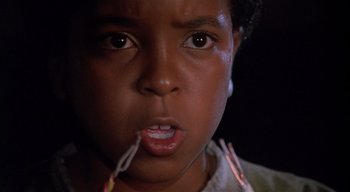 Movie still from “The People Under the Stairs” (1991), directed by Wes Craven – A young boy is holding a pair of paper clips in his mouth; Close Up shot, Low angle