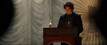 Movie still from “The Personal History of David Copperfield” (2019), directed by Armando Iannucci – A man standing in front of a candle on top of a table; Medium shot, Low angle