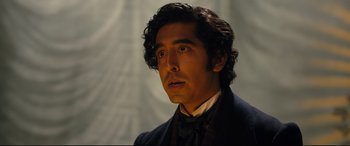 Movie still from “The Personal History of David Copperfield” (2019), directed by Armando Iannucci – A person wearing a suit and tie; Close Up shot, Over the shoulder angle