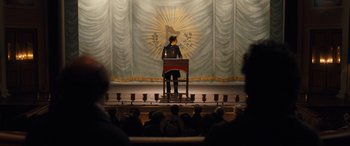 Movie still from “The Personal History of David Copperfield” (2019), directed by Armando Iannucci – A man is standing at a podium on a stage; Wide shot, Low angle