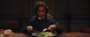 Movie still from “The Personal History of David Copperfield” (2019), directed by Armando Iannucci – A young man is cutting broccoli with a knife and fork; Close Up shot, High angle