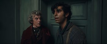 Movie still from “The Personal History of David Copperfield” (2019), directed by Armando Iannucci – Two men standing next to each other near a door; Close Up shot, Over the shoulder angle
