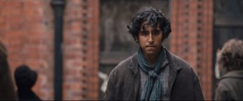 Movie still from “The Personal History of David Copperfield” (2019), directed by Armando Iannucci – A man with a curly hair and a scarf around his neck; Medium shot, Over the shoulder angle