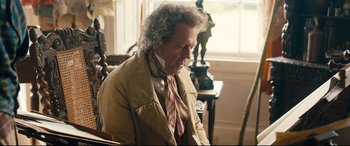 Movie still from “The Personal History of David Copperfield” (2019), directed by Armando Iannucci – An older man sitting in a chair looking at a computer screen; Medium shot, Over the shoulder angle