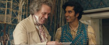 Movie still from “The Personal History of David Copperfield” (2019), directed by Armando Iannucci – Two men are laughing together while one is holding a piece of paper; Medium shot, Over the shoulder angle