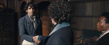 Movie still from “The Personal History of David Copperfield” (2019), directed by Armando Iannucci – Two men shaking hands in front of each other; Medium shot, Over the shoulder angle