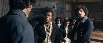 Movie still from “The Personal History of David Copperfield” (2019), directed by Armando Iannucci – A group of men in suits and ties in a room; Medium shot, Over the shoulder angle