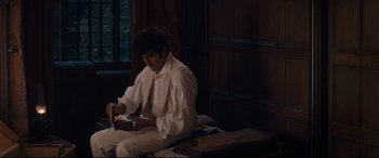 Movie still from “The Personal History of David Copperfield” (2019), directed by Armando Iannucci – A man sitting on top of a bed playing a video game; Medium shot, High angle
