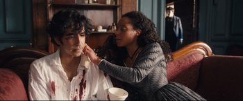 Movie still from “The Personal History of David Copperfield” (2019), directed by Armando Iannucci – A woman putting makeup on a man's face; Medium shot, Over the shoulder angle