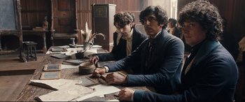 Movie still from “The Personal History of David Copperfield” (2019), directed by Armando Iannucci – A group of people sitting at a table with papers; Medium shot, High angle