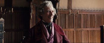 Movie still from “The Personal History of David Copperfield” (2019), directed by Armando Iannucci – An older man in a suit and tie smiling for the camera; Close Up shot, Low angle