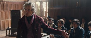 Movie still from “The Personal History of David Copperfield” (2019), directed by Armando Iannucci – An older man in a red jacket is shaking hands with a young man; Medium shot, Over the shoulder angle