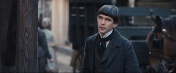 Movie still from “The Personal History of David Copperfield” (2019), directed by Armando Iannucci – A man in a suit and tie standing on a street; Close Up shot, Over the shoulder angle