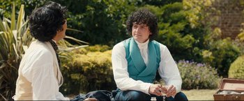 Movie still from “The Personal History of David Copperfield” (2019), directed by Armando Iannucci – A man sitting on the ground with a chess set; Medium shot, Over the shoulder angle