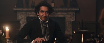 Movie still from “The Personal History of David Copperfield” (2019), directed by Armando Iannucci – A man sitting in front of a fireplace in front of a fireplace; Medium shot, Over the shoulder angle