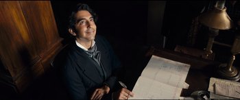 Movie still from “The Personal History of David Copperfield” (2019), directed by Armando Iannucci – A man sitting at a table in front of papers; Medium shot, High angle