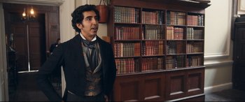Movie still from “The Personal History of David Copperfield” (2019), directed by Armando Iannucci – A man standing in front of a bookcase in a library; Medium shot, Over the shoulder angle