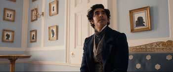 Movie still from “The Personal History of David Copperfield” (2019), directed by Armando Iannucci – A man wearing a suit and tie in front of a door; Medium shot, Over the shoulder angle