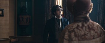 Movie still from “The Personal History of David Copperfield” (2019), directed by Armando Iannucci – A man in a suit and tie standing in a room; Medium shot, Over the shoulder angle