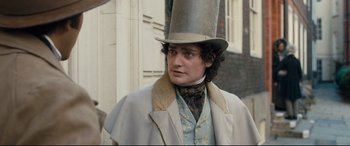 Movie still from “The Personal History of David Copperfield” (2019), directed by Armando Iannucci – A man wearing a top hat standing in front of a building; Close Up shot, Over the shoulder angle